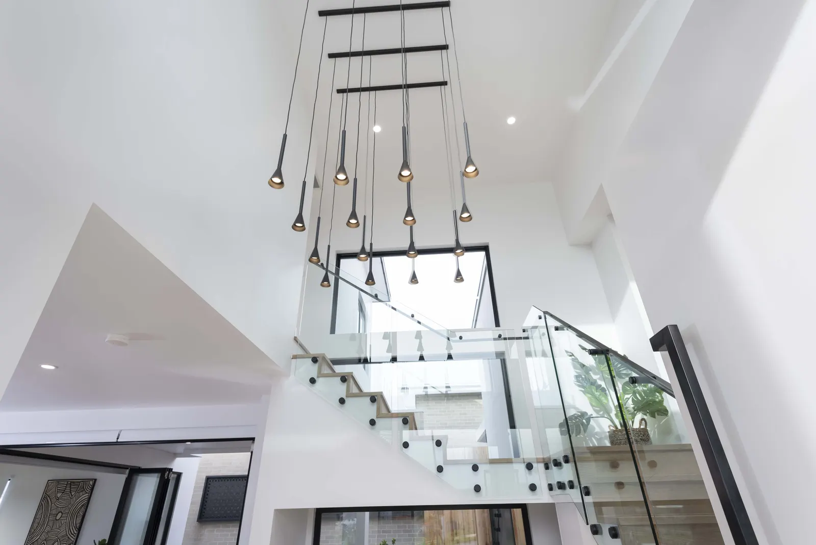 Double height entry void with cascading pendant lights and glass staircase