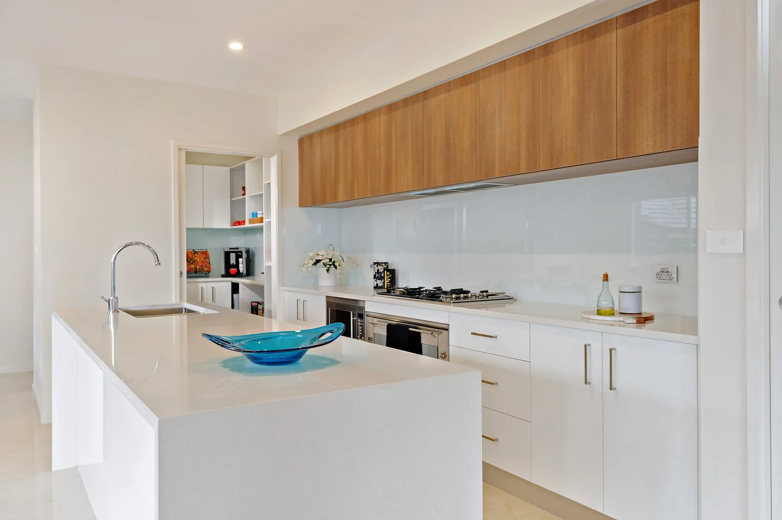 Galley kitchen with timber overhead cabinets, stone island and glass splashback