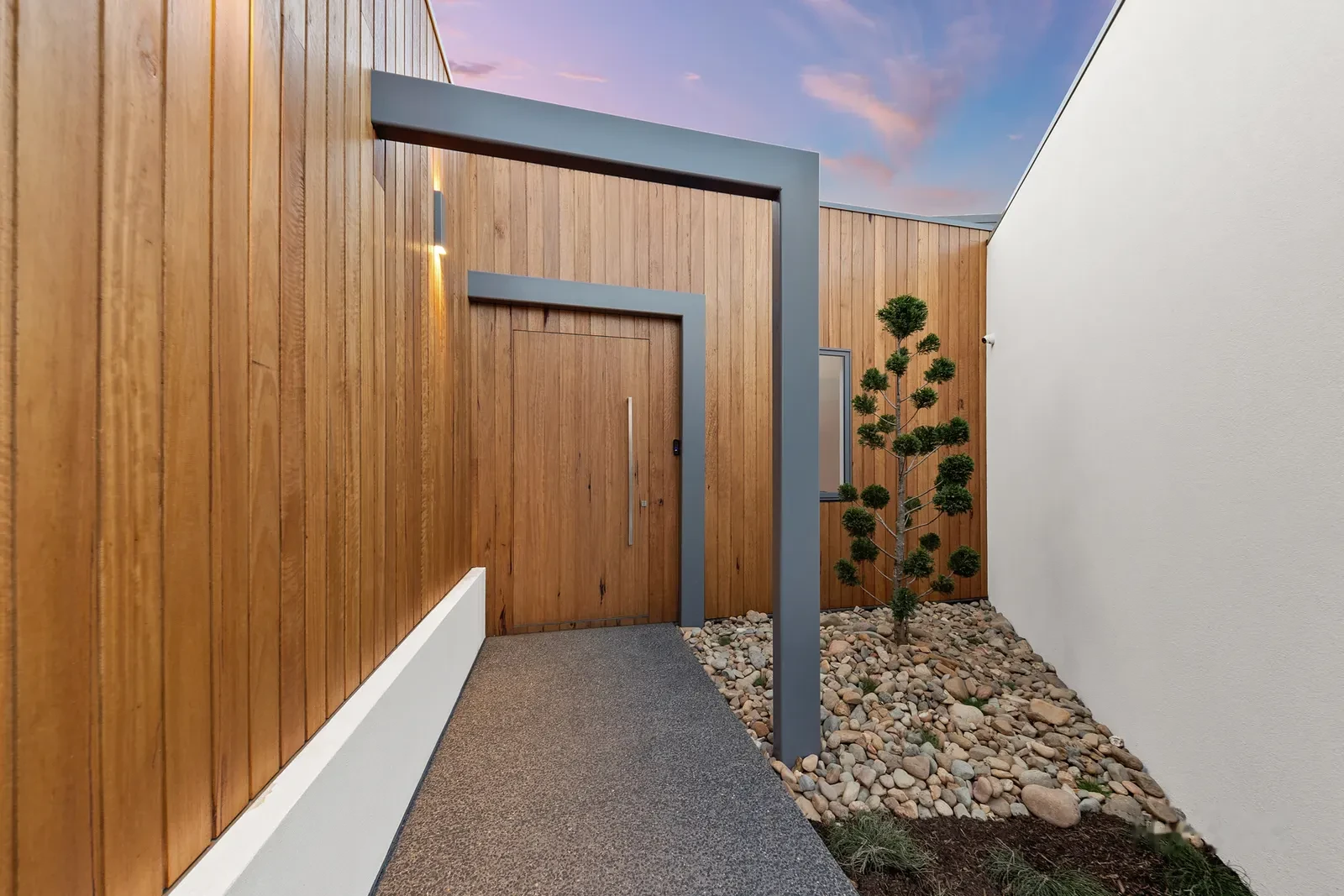 Timber lined entry with steel portal and solid timber front door at dusk