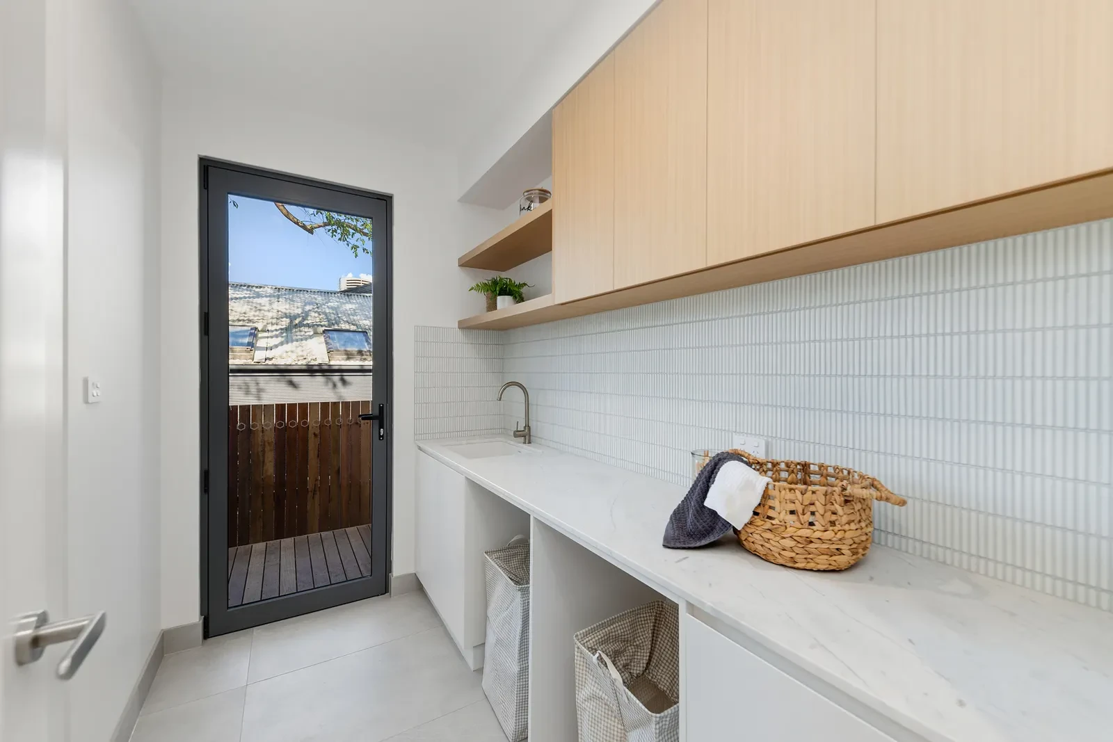 Custom laundry with warm timber cabinetry and tiled splashback